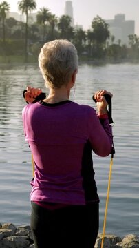 71 year old woman working out in the park with resistance bands. Vertical video.