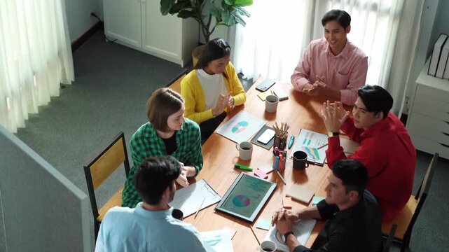 Top view of attractive diverse team clapping hands while project manager present creative idea at meeting room. Diverse team working together planning marketing strategy at meeting room. Convocation.