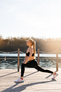 Women exercise on wooden deck by the water during sunny day enjoying fitness in beautiful nature