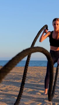 Attractive woman working out on the beach with battle ropes at sunset. Slow Motion. Vertical video.