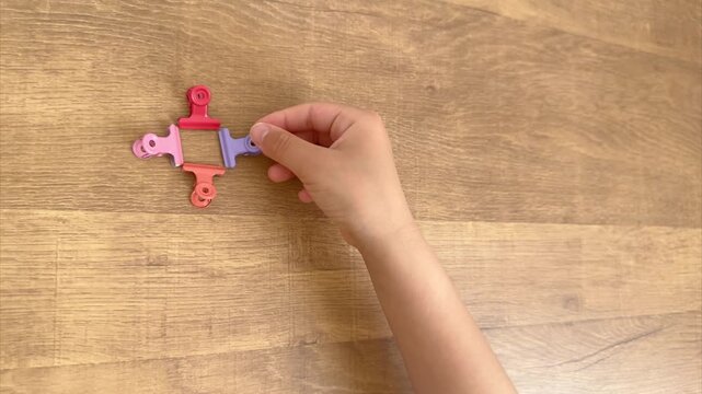 Child Hand Placing the Fourth Colorful Clip in a Regular Pattern from an Oblique Overhead View, 4K Silent Video