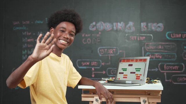 Smart african boy use laptop to code program and turn around to wave hand. Cute high school stident coding engineering prompt or program system at blackboard in STEM technology classroom. Edification
