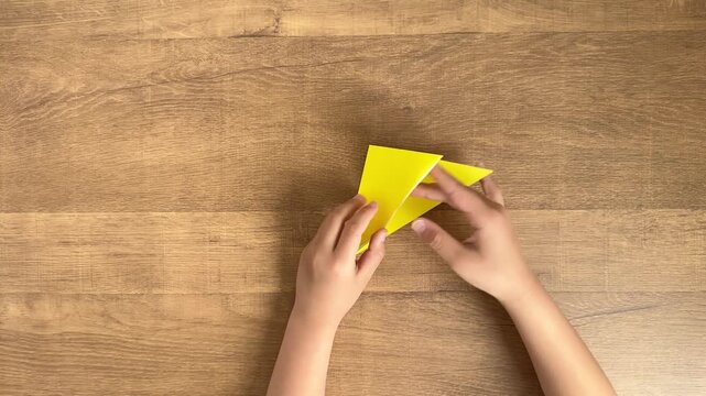 Child Hands Making a Squash Fold with Yellow Origami Paper from a Top-Down View, Step Four, 4K Silent Video