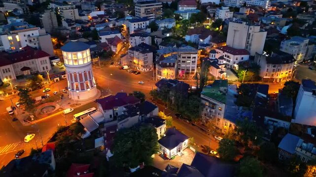 Cinematic high angle night view of the illuminated Bucharest fire tower in Romania. Iconic historic brick landmark surrounded by glowing city lights.