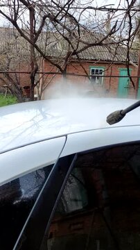 Washing white car with pressure washer, first person view, vertical
