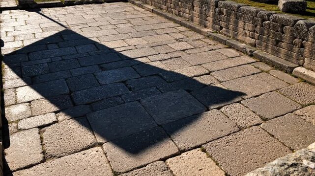 Long shadow of a person cast on sunlit stone pavement