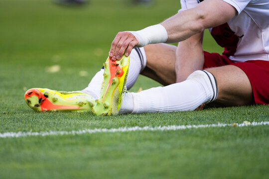 A soccer player sitting on the pitch strains his foot due to a leg cramp.