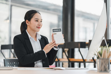 Obraz premium Businesswoman holding a calculator while working at her desk in a modern office