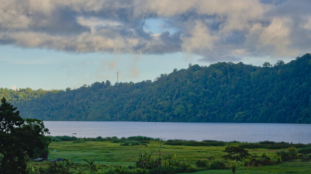 Beautiful panoramic view of Lake Buyan in Bali under a cloudy sky, featuring green valleys, hills, and peaceful natural waterfront.