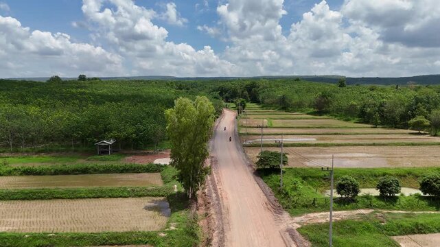Aerial view of two motorcycles riding on a rural dirt road through lush green mountains.