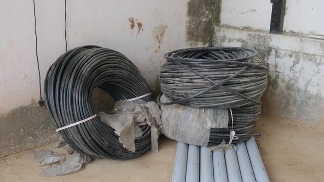 Large coils of black agricultural HDPE pipe and gray conduit pipes stored on the ground
