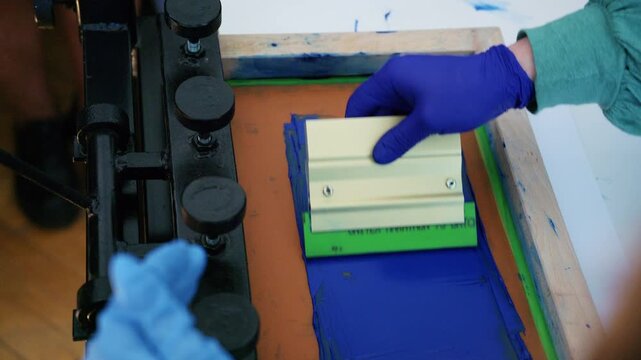 Worker using a squeegee to spread ink across a screen printing frame during textile production