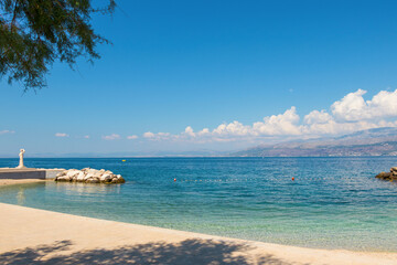 Fototapeta premium Scenic coastal view of Postira village on Brac Island, Croatia. Crystal clear turquoise water of the Adriatic Sea, rocky beach, and distant mountains on the horizon under a bright blue summer sky