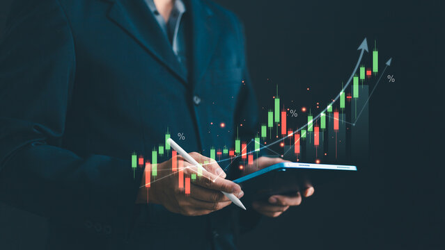 Businessman holding digital tablet and stylus pen with growing financial stock market candlestick chart graph. Business growth investment analysis, economy and data technology concept.
