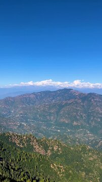 Snow capped Himalayan mountain range visible from Uttarakhand above rolling forested hills. Clear blue sky high altitude landscape, wilderness scenery, travel destination garhwal trekking adventure UK