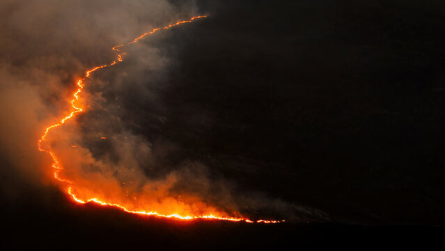 Aerial view of an active wildfire spreading across a dark landscape with glowing fire lines dense smoke and visible environmental impact during a forest fire.