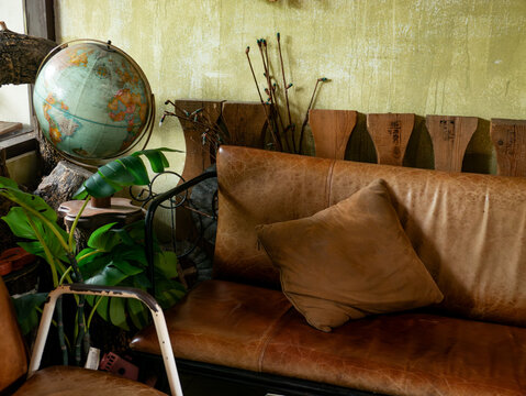 Vintage eclectic cafe interior with distressed leather sofa globe world map monstera plant rustic wood and green wall decor