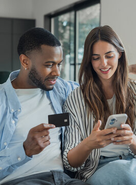 Young couple on a sofa completing an online purchase with a credit card and smartphone, using mobile banking app for secure, convenient at-home digital payments and shopping
