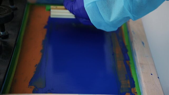 Worker using a squeegee to spread ink across a screen printing frame during textile production