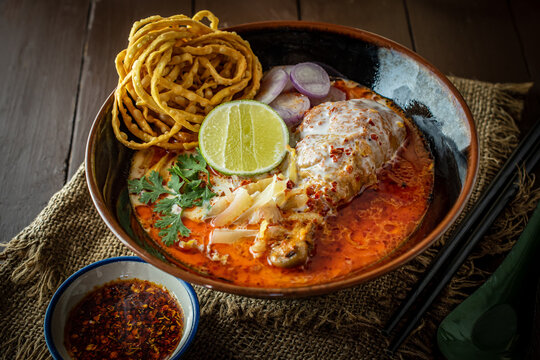 Traditional Khao Soi Kai, a Northern Thai chicken egg noodle curry with crispy noodles, lime, and red onions in a dark bowl, captured in a rustic food photography style for Asian cuisine design.