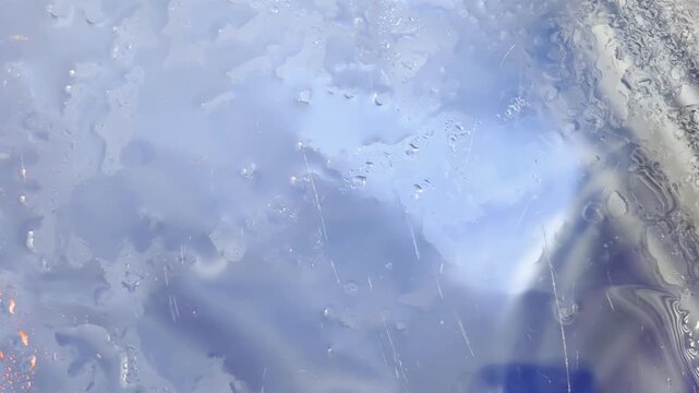 Freezing water transforming into ice crystals on a cold winter window, creating a beautiful abstract frosty pattern with liquid condensation and melting droplets