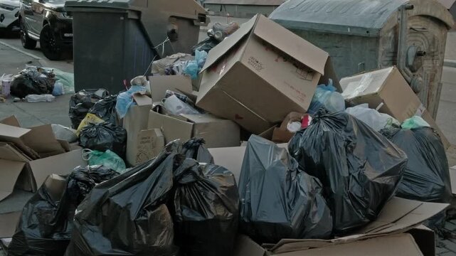 Wide shot of overflowing garbage dumpster and piled trash bags on a city sidewalk horizontal view