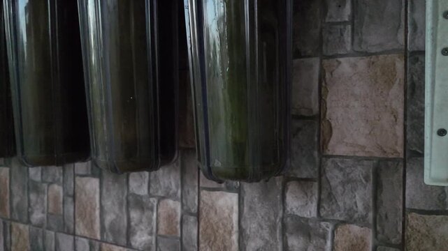 Close up shot of water droplets dripping from the bottom of a contaminated 10-inch water filter housing tank mounted on a stone wall. Represents plumbing system leakage and defective maintenance issue