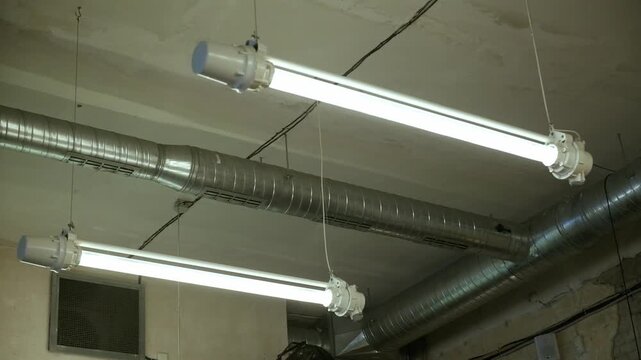 Low angle shot of industrial fluorescent light fixtures and ventilation ducts on a ceiling horizontal view