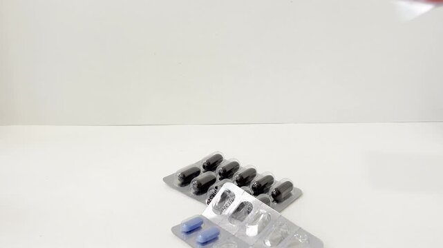 Hand placing various blister packs of pills, capsules, and lozenges on a white background representing medication, health supplements, and daily vitamin regimen
