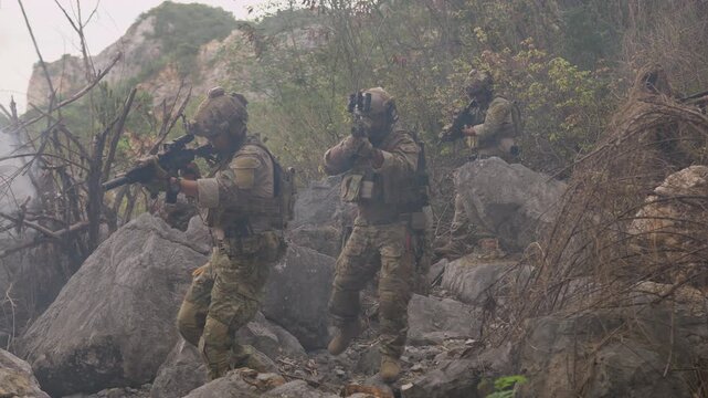 A special forces squad executes a tactical maneuver through smoky, rocky terrain, engaging in a military operation to secure a hostile jungle environment.