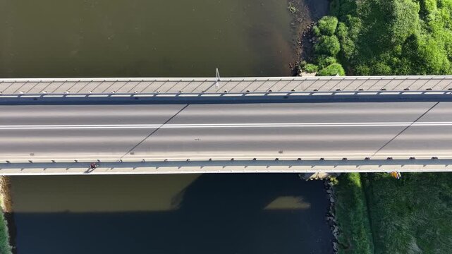 Top down aerial view of a white car driving along a modern concrete bridge over a river. Minimalist highway road infrastructure design at sunny day.