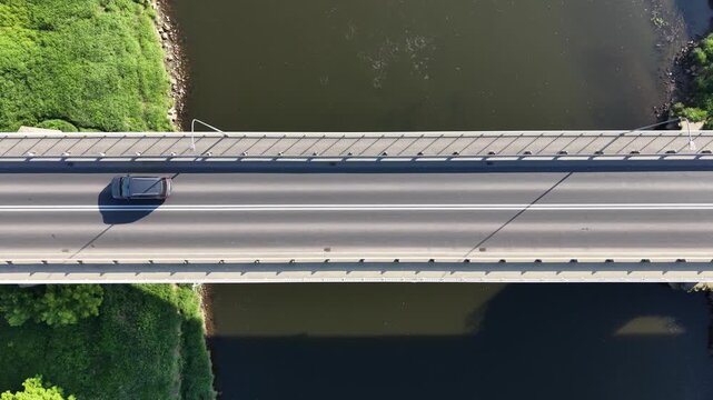 Top down aerial view of a white car driving along a modern concrete bridge over a river. Minimalist highway road infrastructure design at sunny day.