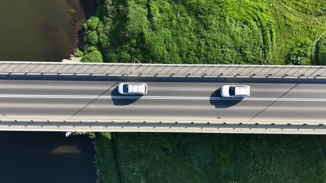 Top down aerial view of a white car driving along a modern concrete bridge over a river. Minimalist highway road infrastructure design at sunny day.