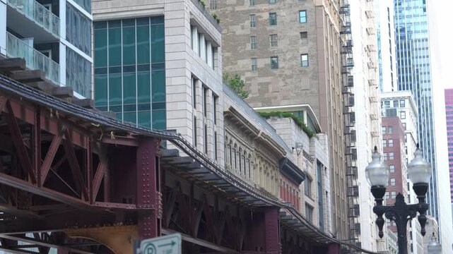 Elevated train tracks curve through dense Chicago downtown architecture. Skyscrapers and historic buildings create layered urban cityscape.
