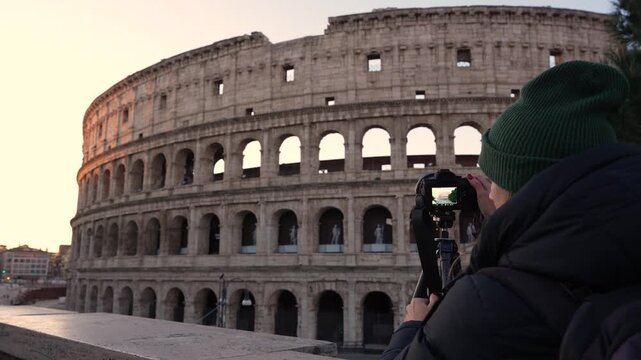 A Female Photographer Shoots Sunrise at the Roman Colosseum in Rome, Italy. European Travel Hat and Coat Tripod Professional Warm Light Tourist