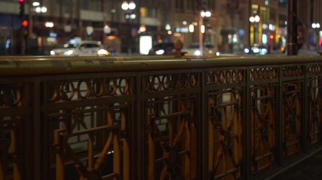 Chicago street scene at night with decorative metal bridge railing and blurred city lights in the background. Urban infrastructure and traffic create a warm illuminated evening atmosphere.