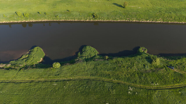 Top down aerial view of a green riverbank and dark river water. Abstract nature background of a winding river coast from drone.