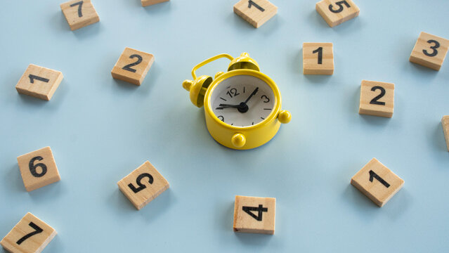 Angled shot of a yellow mini alarm clock placed among scattered wooden number tiles, concept of managing time, tracking deadlines, and financial periods.