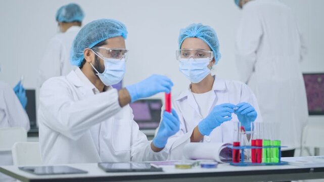 Collaborative team of medical professionals wearing protective gear carefully inspect test tubes filled with fluids during an important pharmaceutical development proces