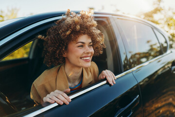 A joyful woman leans out of a car window, enjoying sunny outdoors. A candid lifestyle shot with...