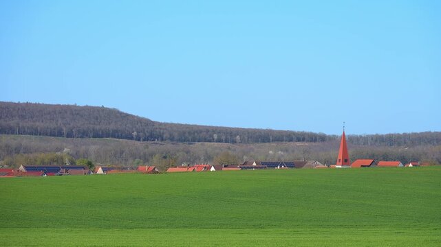 Kleine Ortschaft mit Kirche im Hintergrund eines gro&szlig;en gr&uuml;nen Feldes unter klarem Himmel, Ergersheim, Landkreis Neustadt an der Aisch-Bad Windsheim, Mittelfranken, Bayern, Deutschland