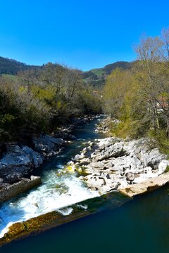 Crystal clear 
river surrounded by lush green vegetation in Puente 
Viesgo, Cantabria, northern Spain. Peaceful rural 
landscape of the Cantabrian valley
