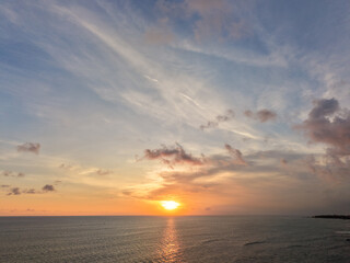 Fototapeta premium Aerial view of a beautiful golden sunset over the calm ocean horizon with clouds