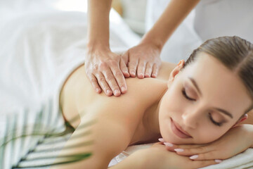 Fototapeta premium Massage therapy for girls wellness and beauty in spa salon. Hands of therapist touch back muscles for relaxation and body care of client, young woman relaxing, lying with eyes closed and smile