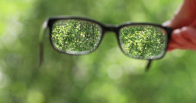 Clear vision through spectacles in hand on blurred nature background, choosing glasses for sharp view and eyesight correction for focused view.