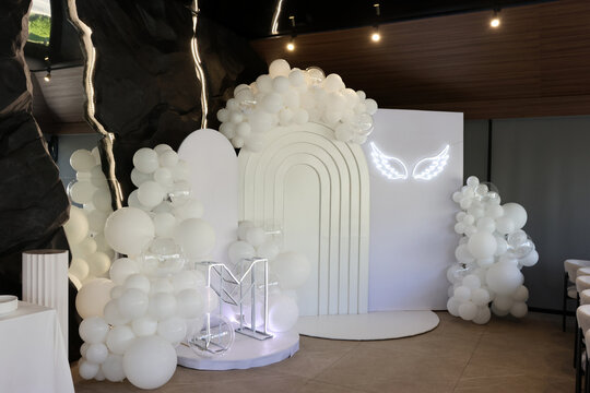 Festive photo zone with white balloons, decorative arch and illuminated elements prepared for a wedding event.