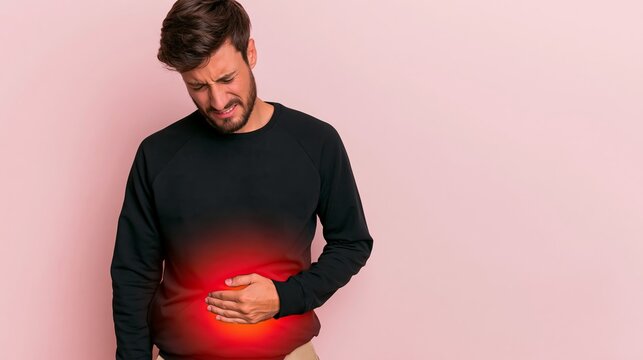 Young man experiencing severe abdominal pain, clutching stomach with highlighted discomfort area on pink background