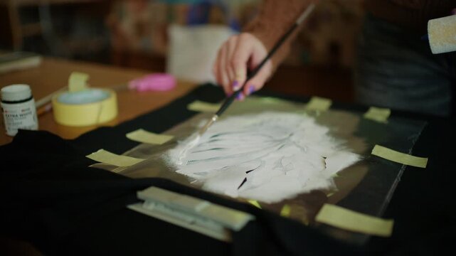 Hands using a craft roller to evenly spread adhesive material over a stencil design