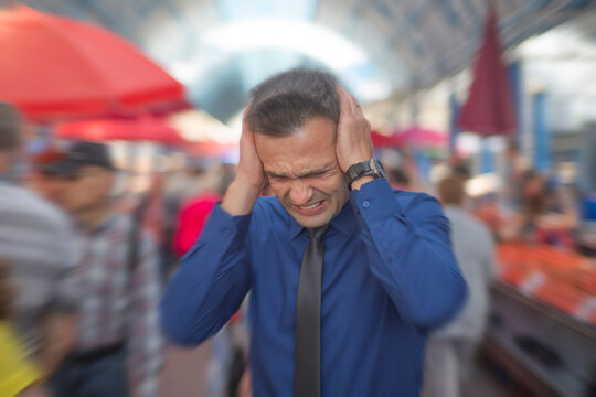 Stressed businessman suffering from panic attack or migraine on crowded city street with copy space