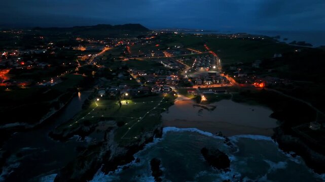 Drone view of a crescent beach and illuminated coastal village in Santander Spain at twilight